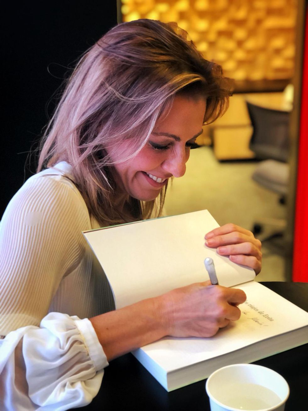 la periodista, con un bolígrafo, firma una de sus obras con una gran sonrisa