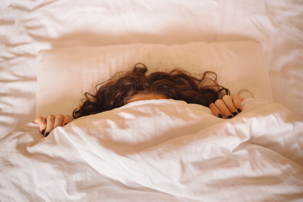 angry woman hides under white blanket, only her long curly hair and dark manicured hands are visible