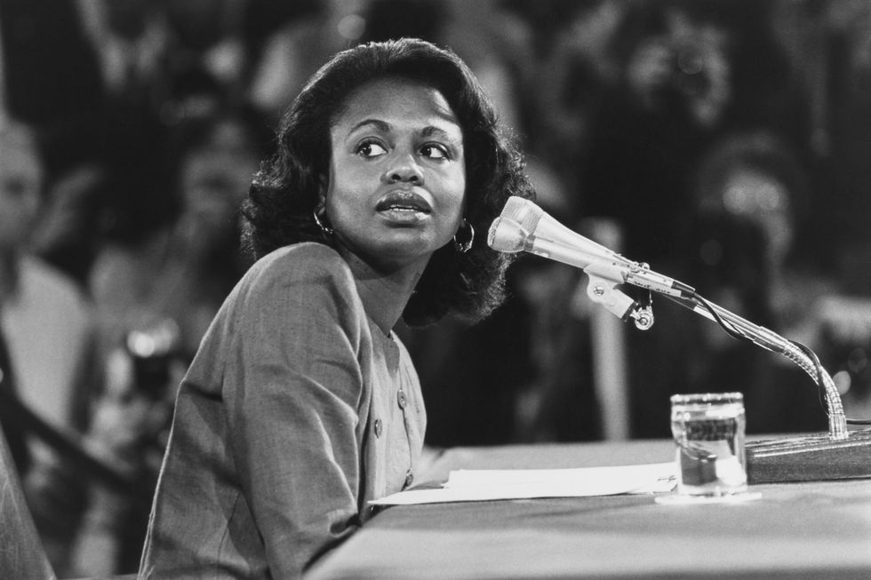 a black and white photo of anita hill sitting at a table and speaking into a microphone before the united states senate
