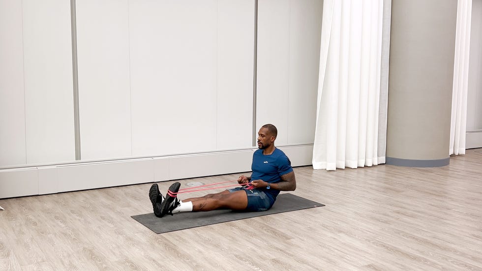 man sitting on an exercise mat performs ankle flexion and extension with a resistance band