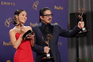 anna sawai and hiroyuki sanada stand in front of a purple backdrop and pose for photos, she holds an emmy trophy with both hands by her face and smiles, he holds an emmy trophy in each hand and smiles