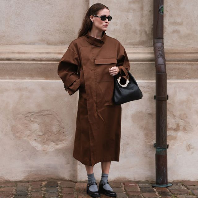 a woman stands against a wall wearing a coat and mary janes in a guide to the best mary janes for women 2023
