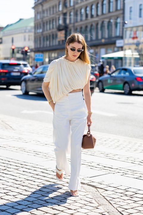 a woman wearing a draped cream blouse and white trousers with white flip flop heels during copenhagen fashion week in a roundup of cute summer outfits 2023