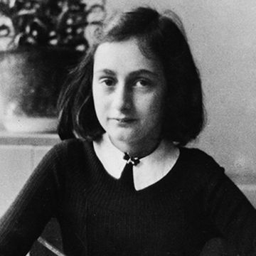 anne frank looks at the camera, she wears a dark sweater over a light colored collared shirt