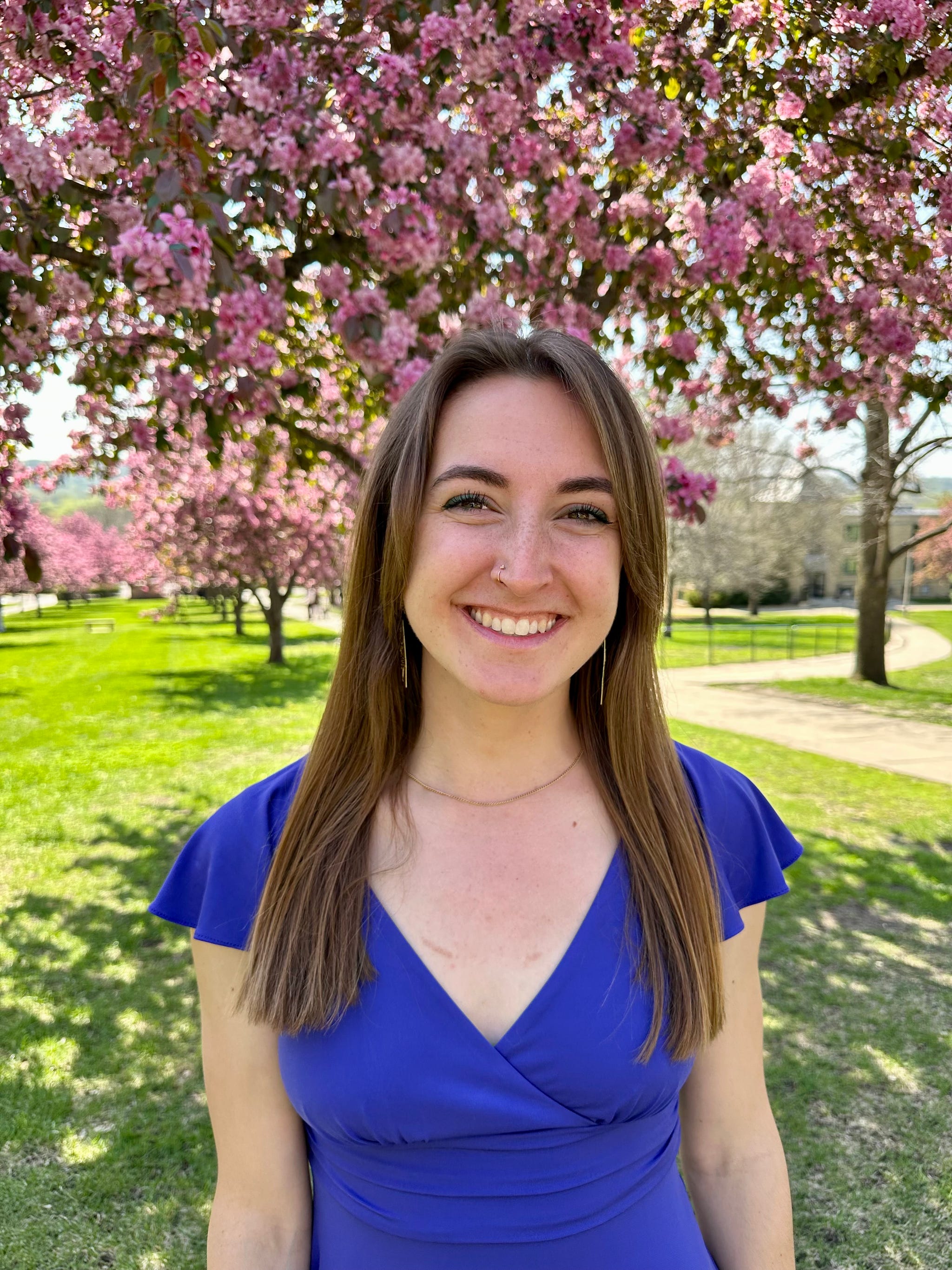 a woman stands in a park with blooming pink trees in the background