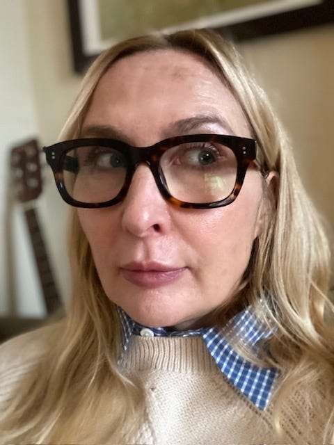 person wearing sunglasses and a sweater with a blue checkered collar sitting indoors