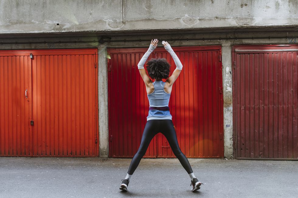 Anonymous Female Athlete with an Afro Haircut Doing Jumping Jacks Outdoors