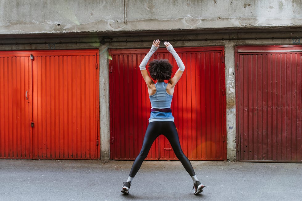 Anonymous Female Athlete with an Afro Haircut Doing Jumping Jacks Outdoors