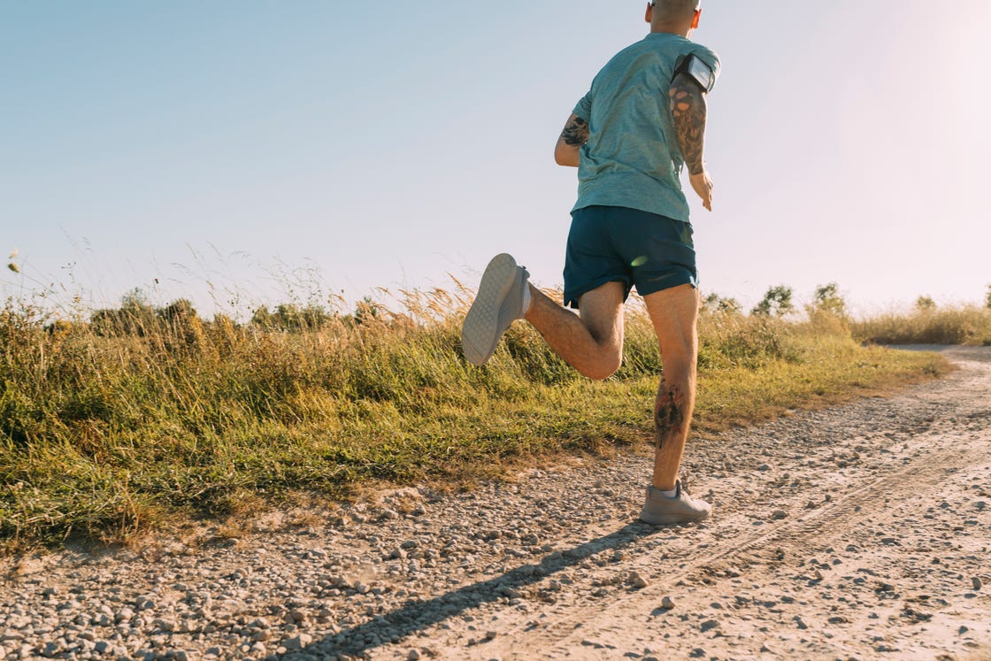 anonymous white sportsman running on a dirt road on a sunny day