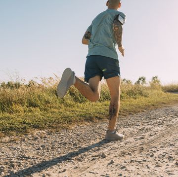 anonymous white sportsman running on a dirt road on a sunny day