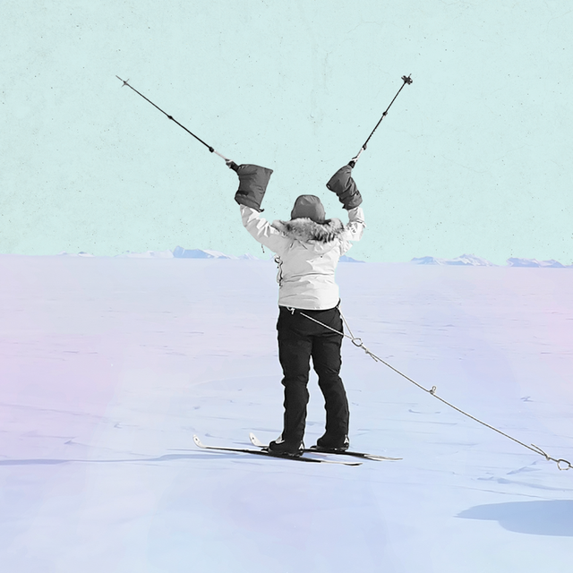 a woman standing in antarctic snow with two ski poles in her hands raised over her head in triumph