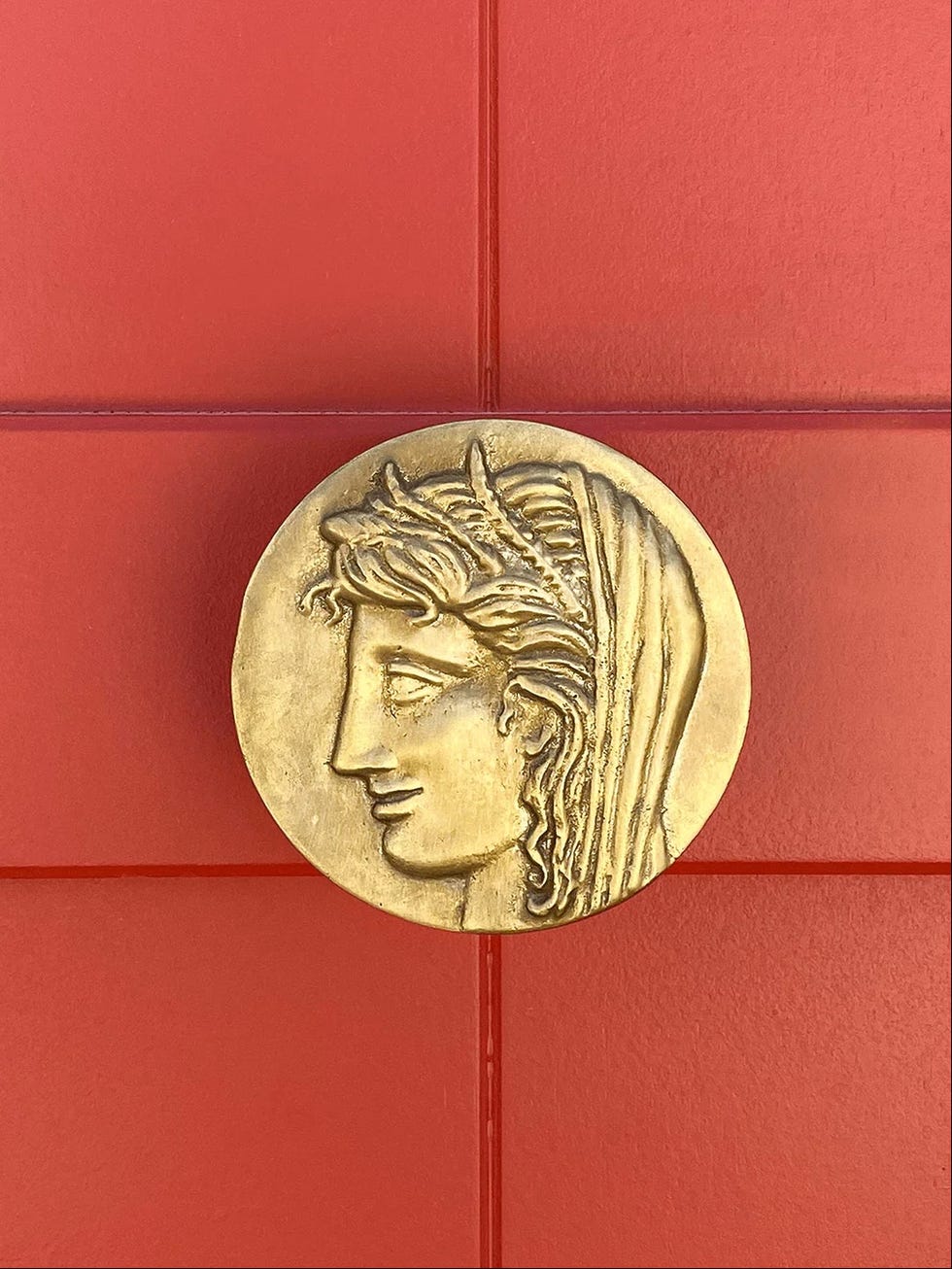 a bronze circular plaque mounted on a red wall depicting intricate detailing of a horses head