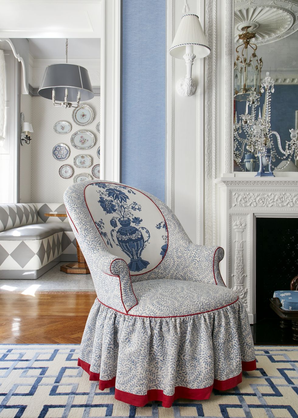 a blue and white upholstered chair sits by a fireplace and you can see a leather banquette in the background with antique china hung on the wall