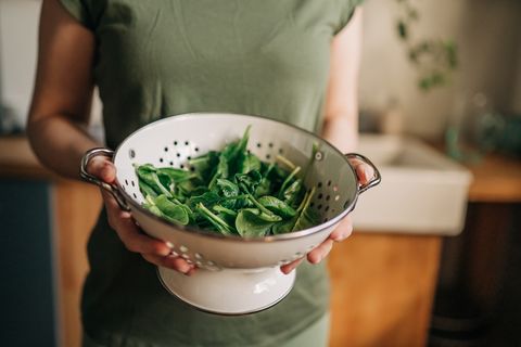 green vegan breakfast meal in bowl with spinach, arugula, avocado, seeds and sprouts girl in leggins holding plate with hands visible, top view clean eating, dieting, vegan food concept