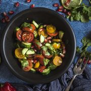 fresh salad with tomato, cucumber and herbs, flat lay from above  the salad is in a black bowl and there are other bowls with ingredients around it the table is decorated with lime, chili and cilantro