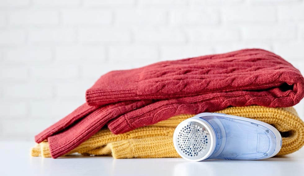 an electric fabric shaver lying next to pile of sweaters