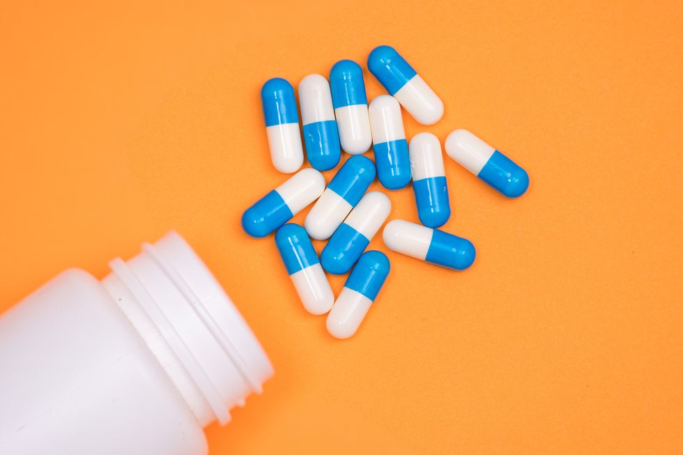 antibiotic medical drug capsule falling from bottle on  orange background