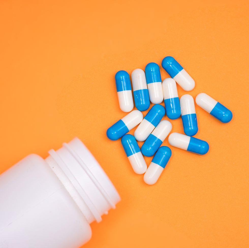 antibiotic medical drug capsule falling from bottle on  orange background