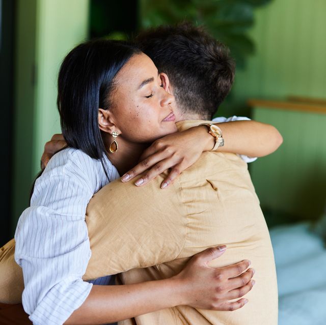 young woman hugging her husband while at home sitting on their bed