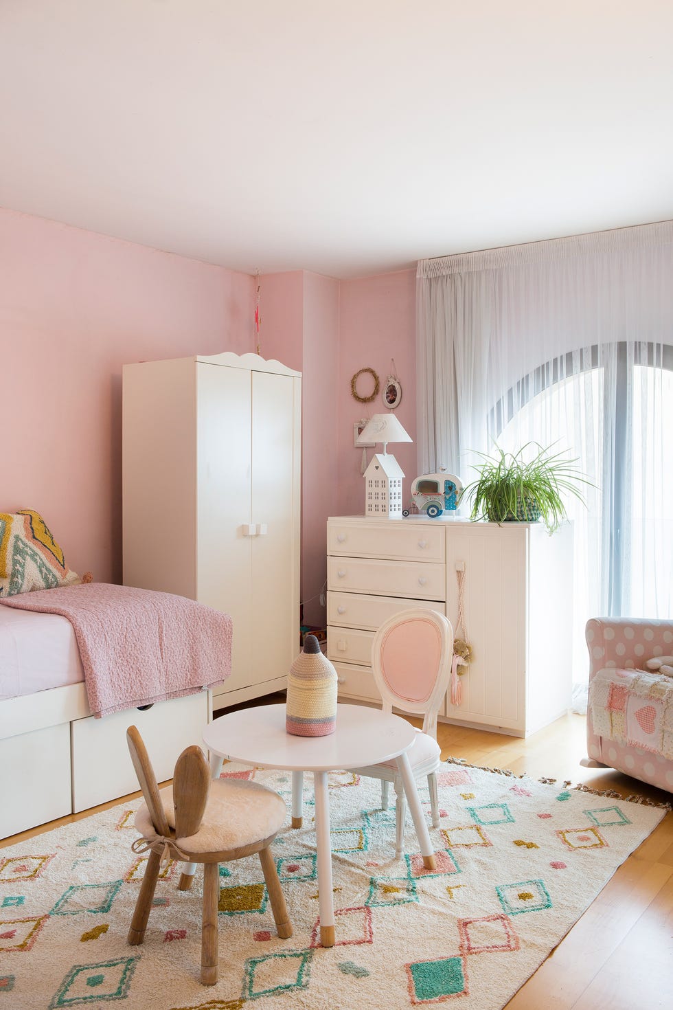 dormitorio infantil con zona de juegos y rincón de lectura decorado en tonos rosas