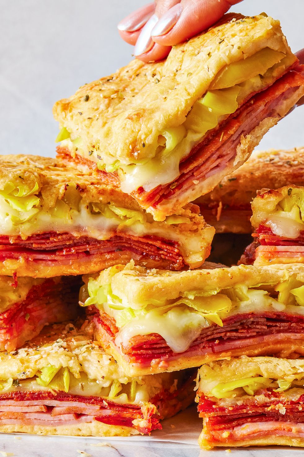stacked sandwiches with layers of ham, pepperoni, cheese, and pepperoncinis between crescent dough