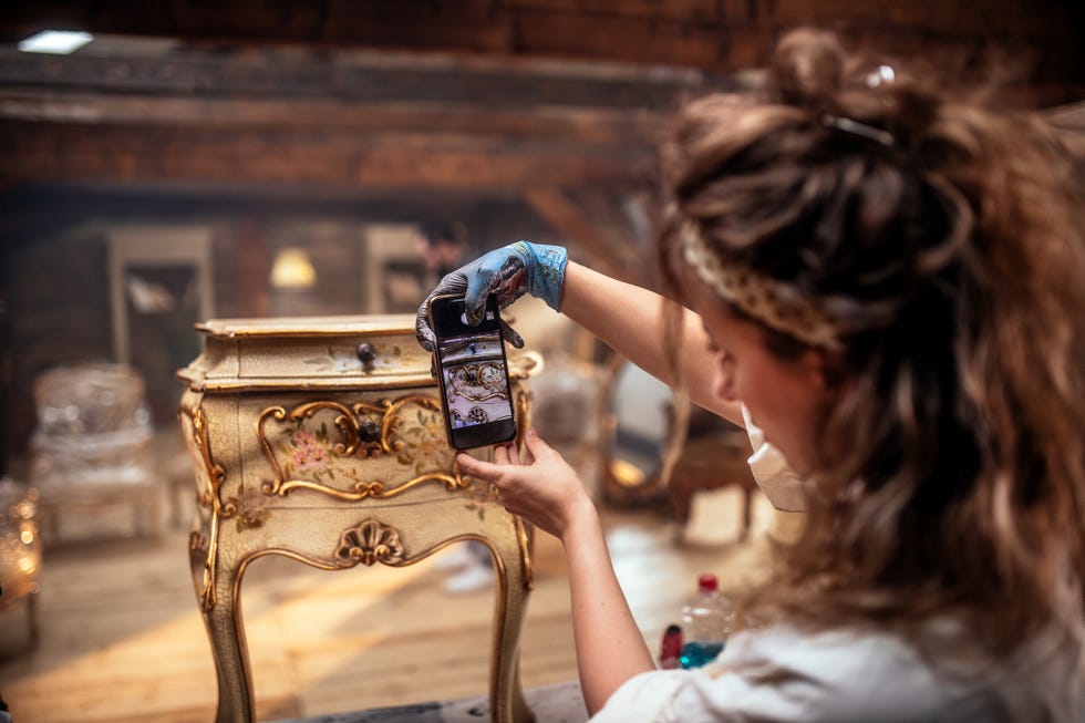 antique shop owner takes pictures of furniture for sale with his mobile phone