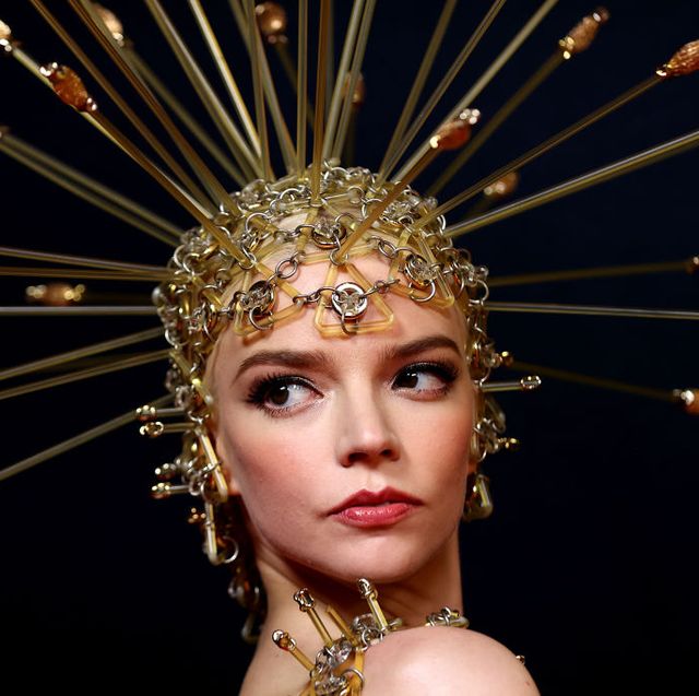anya taylor joy wearing a gold dress and a headdress piece with embellishments sticking out