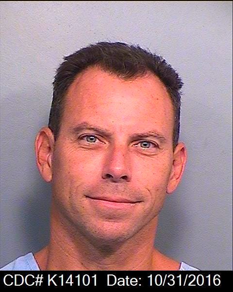 erik menendez slightly smiles at the camera in this headshot, his blue shirt is just visible