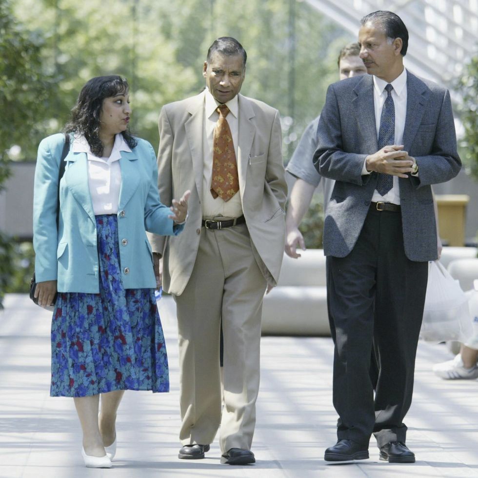 a woman and two men walk inside a sunlight atrium, they wear formal clothes and talk to other another