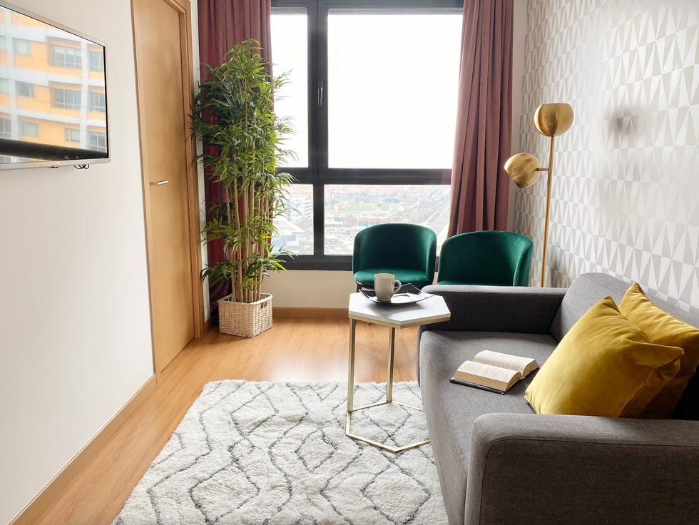 salón moderno con sofá gris, mesa auxiliar de mármol, papel pintado geométrico y butaca de terciopelo verde con lámpara de pie dorada