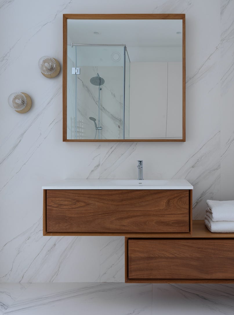 baño con pared y suelo de mármol y mueble de lavabo de madera suspendido