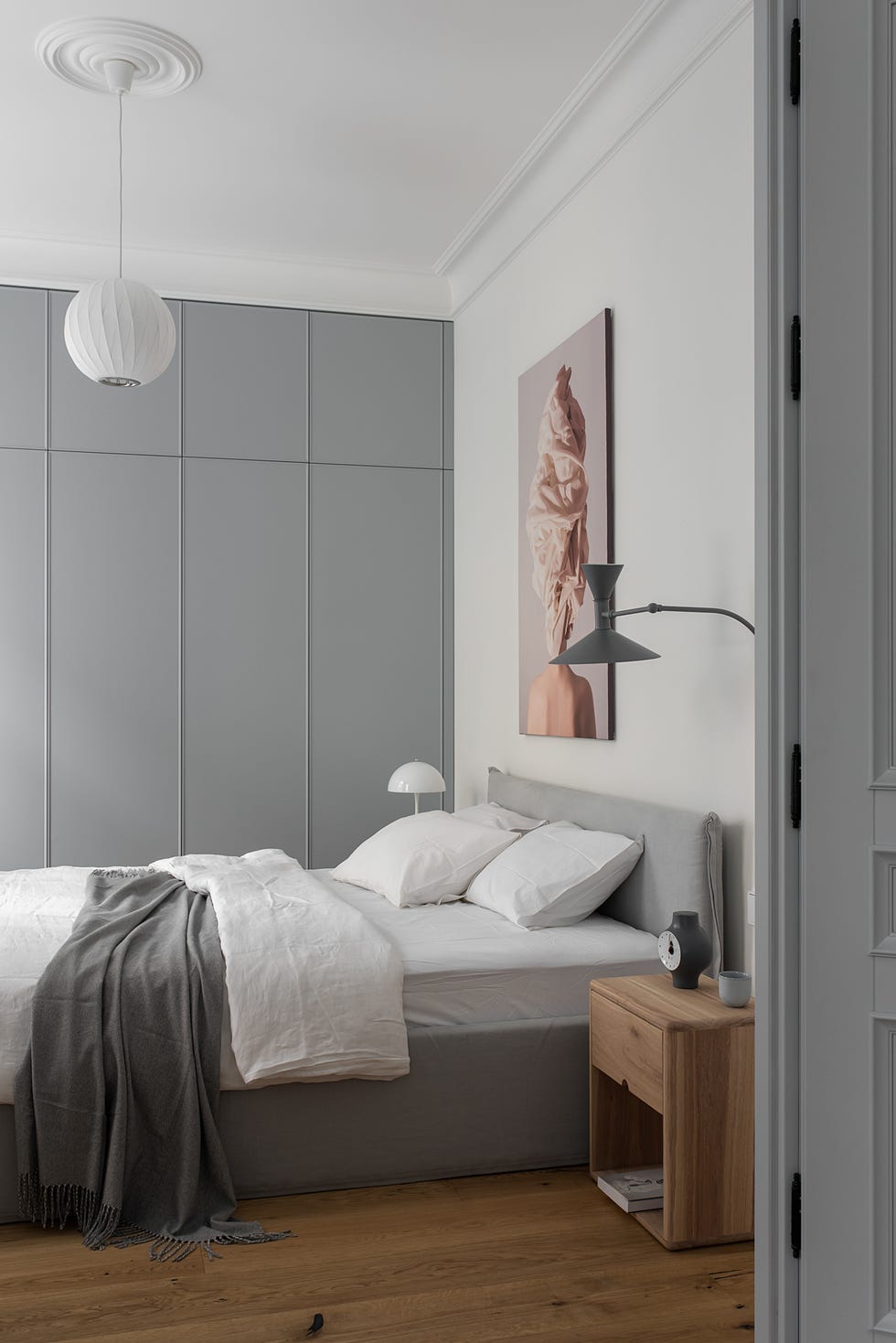 dormitorio nórdico decorado en gris con mesita madera y cuadro sobre la cama