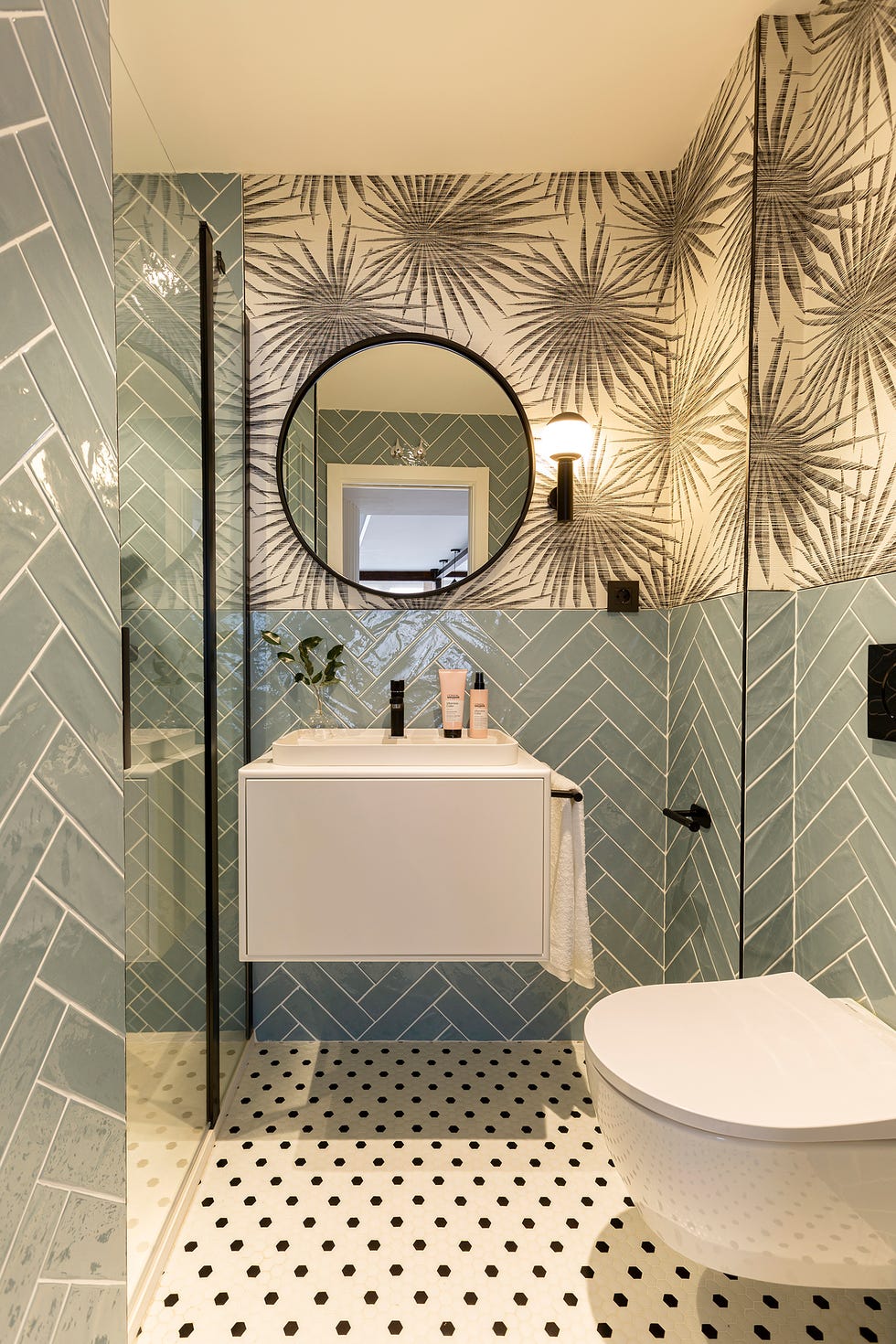baño con azulejos azules en espiga y papel pintado con motivos negros