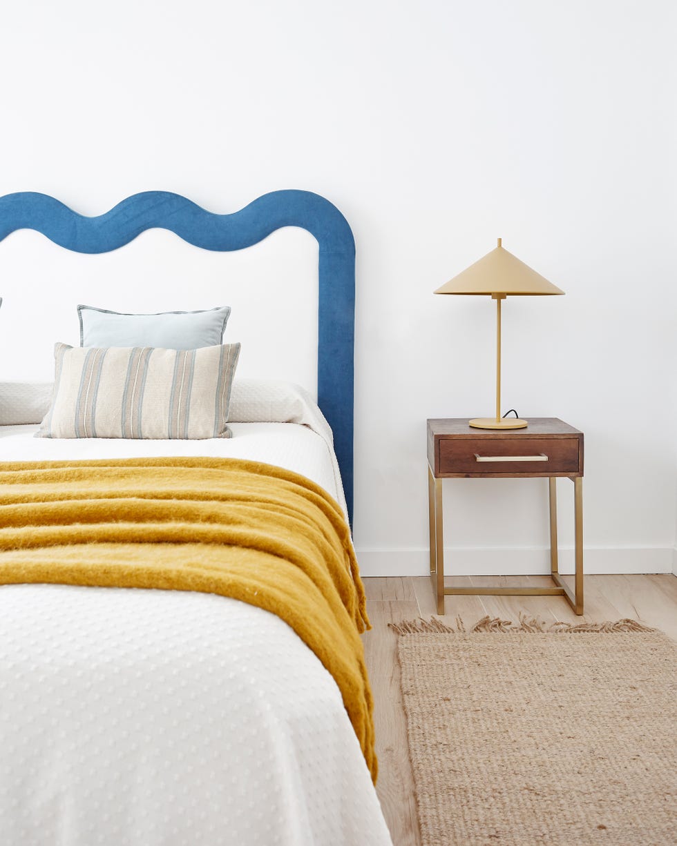 dormitorio de estilo mid century con cabecero con diseño de ondas tapizado en blanco y azul y mesita de madera y latón