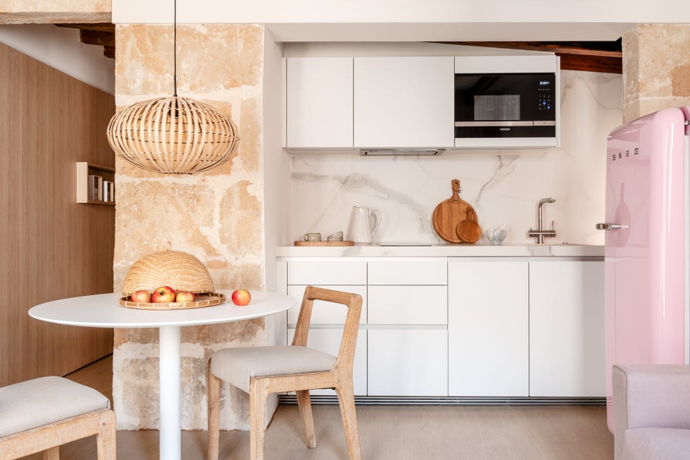 cocina con armarios blancos, frigorífico rosa, muro de piedra vista y mesa de comedor redonda con sillas de madera