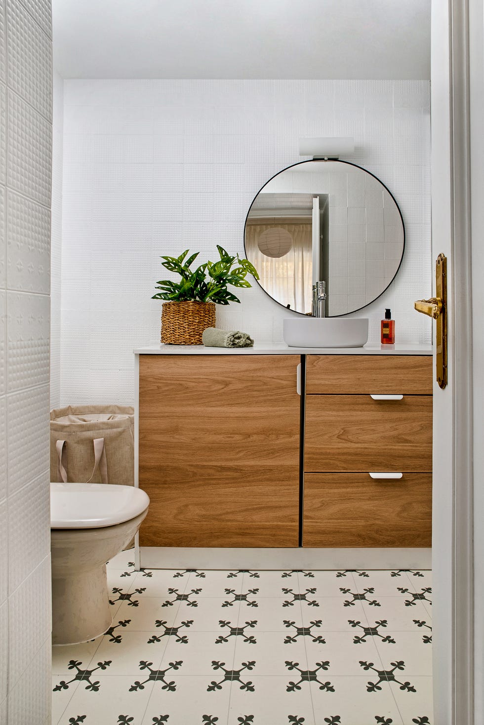 baño con mueble de madera, espejo redondo y baldosas geométricas