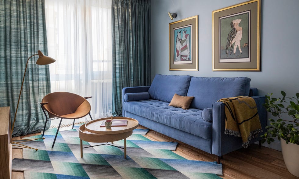 Sofá azul de terciopelo, alfombra de rayas zig zag y rincón de lectura con butaca y lámpara de pie