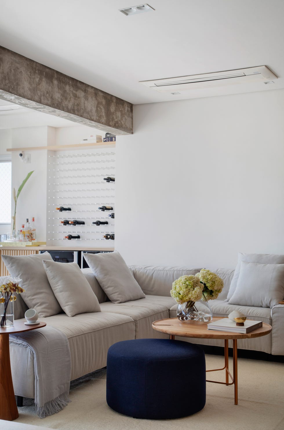 salón con sofá en l de color gris, puf azul marino y mesa de centro redonda de madera