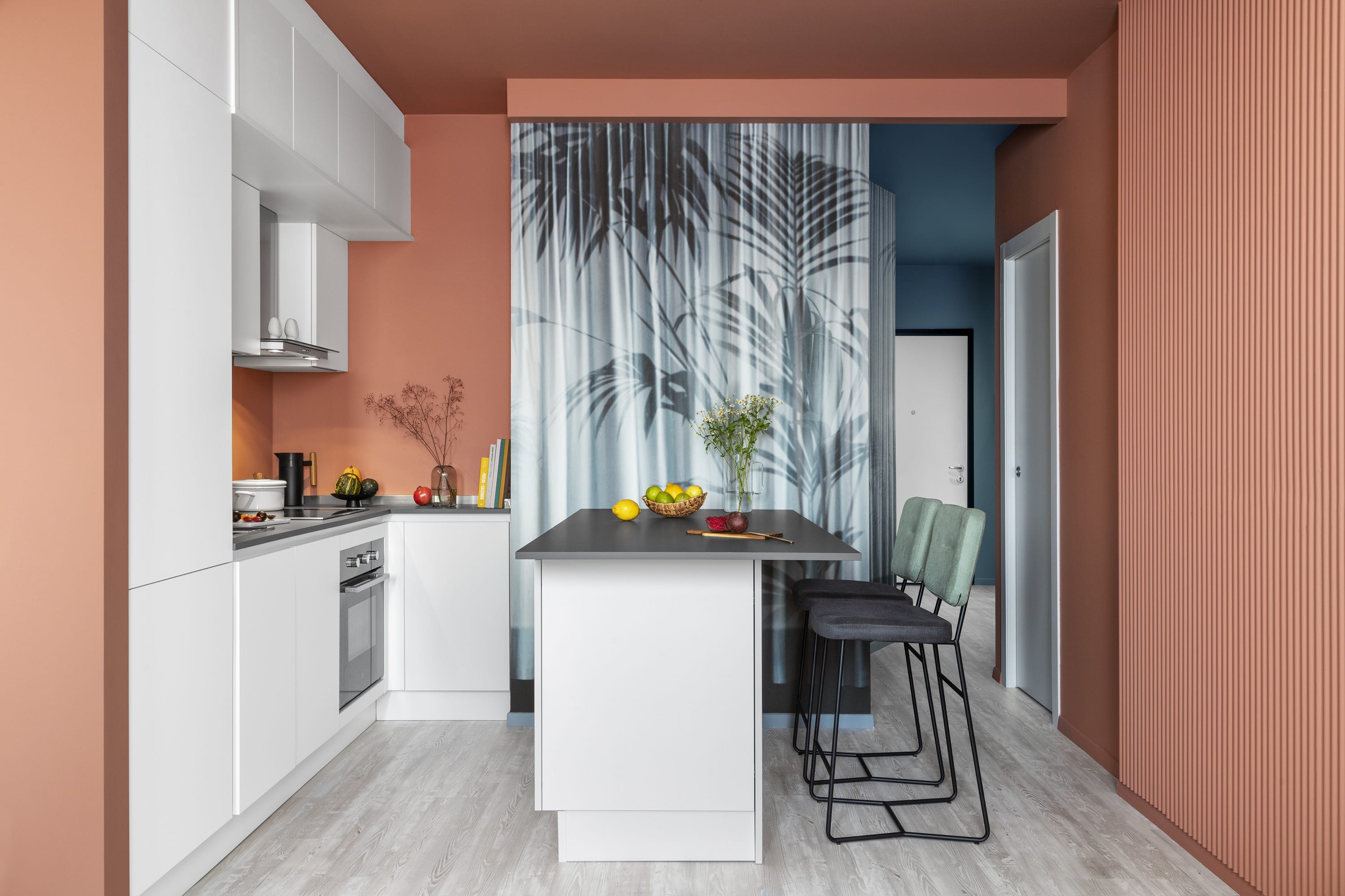 cocina moderna abierta con isla central, molduras decorativas en color teja y cortina con dibujos de palmeras