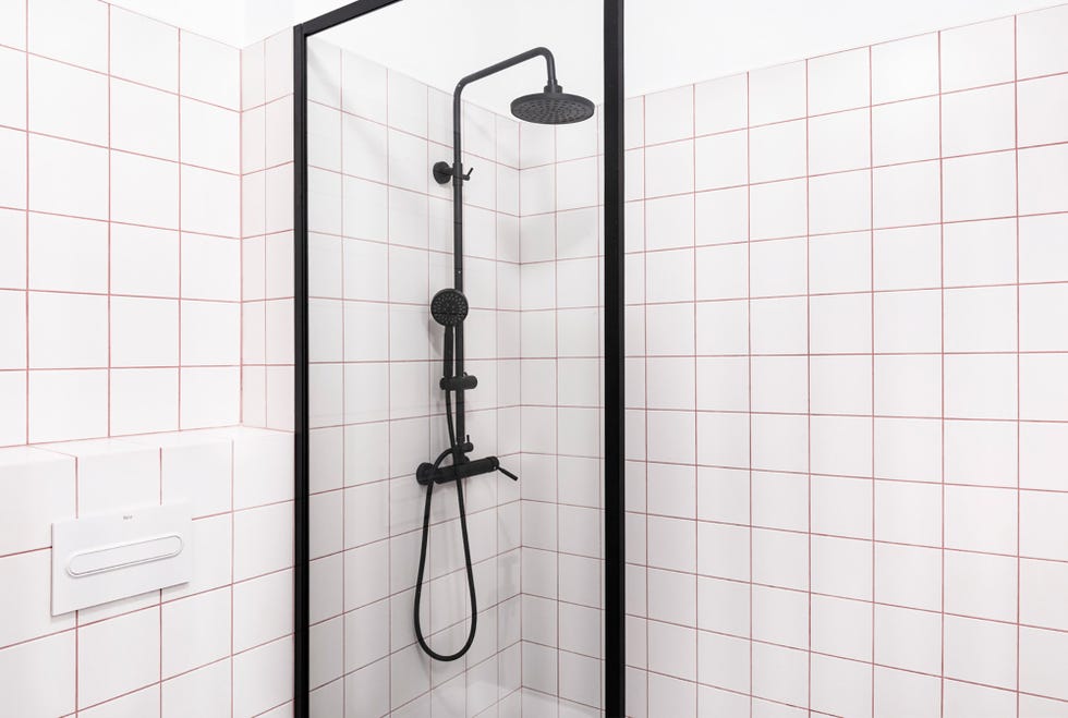 Baño con azulejos blancos y juntas rojas, y grifería de la ducha en negro mate