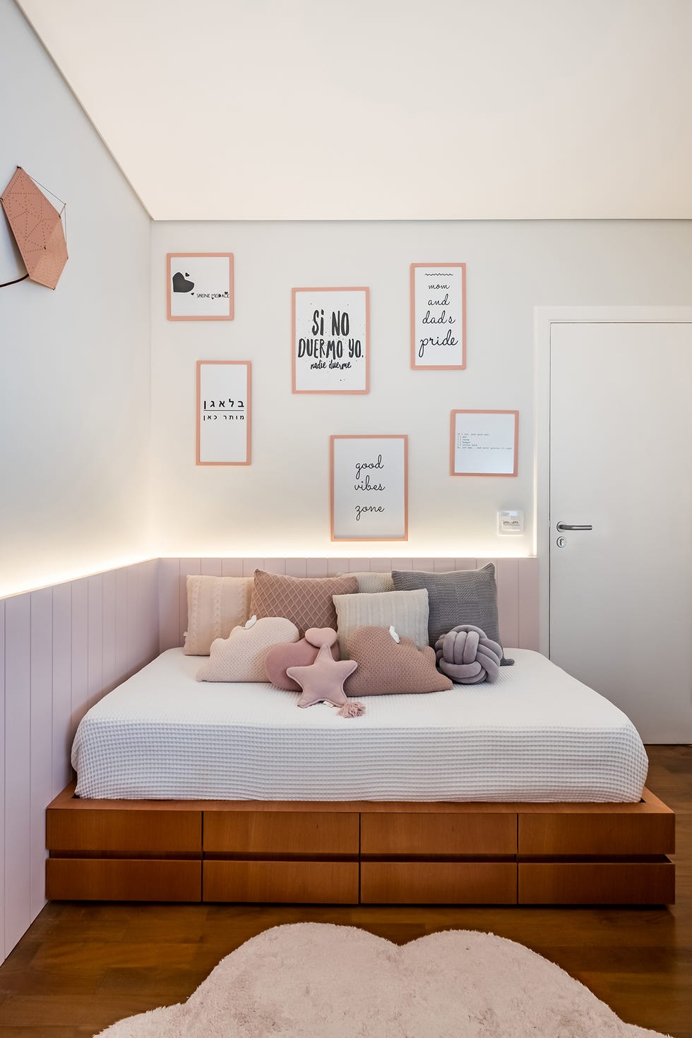 cama infantil con estructura de madera y cojines en tonos rosas