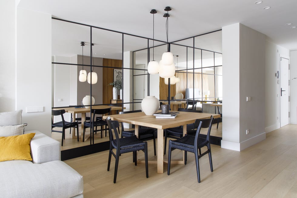 mesa de comedor de madera, sillas negras y paredes de espejo con cuarterones