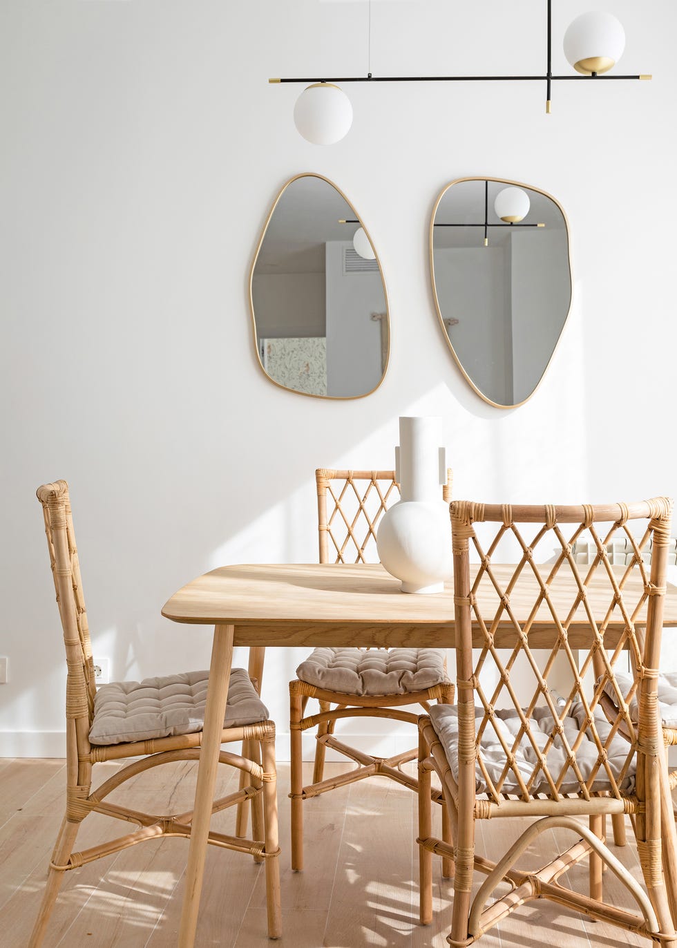 mesa de comedor de madera, sillas de ratán y espejos de pared con forma orgánica