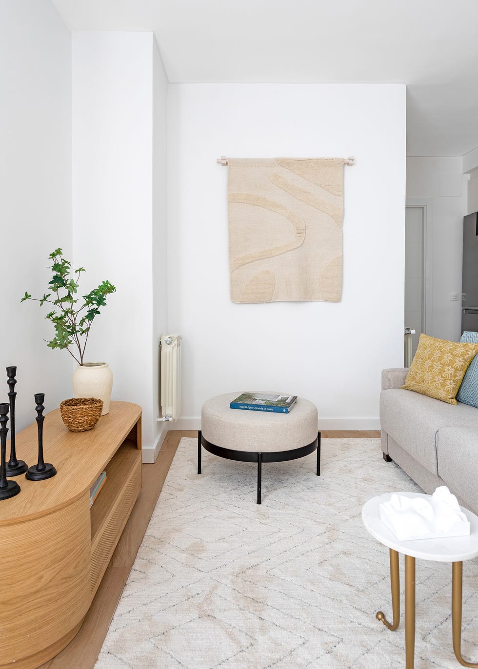 salón moderno con mueble de tv de madera y forma ovalada, mesa auxiliar de mármol y latón y puf tapizado en gris sobre alfombra con diseño a rombos