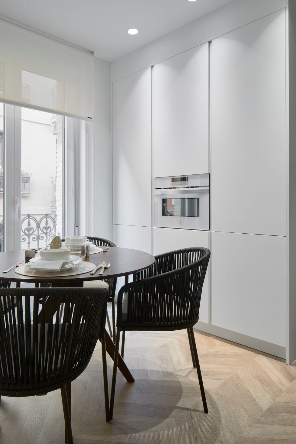 armarios de cocina blancos sin tiradores y office con mesa redonda y sillas de cuerda negra