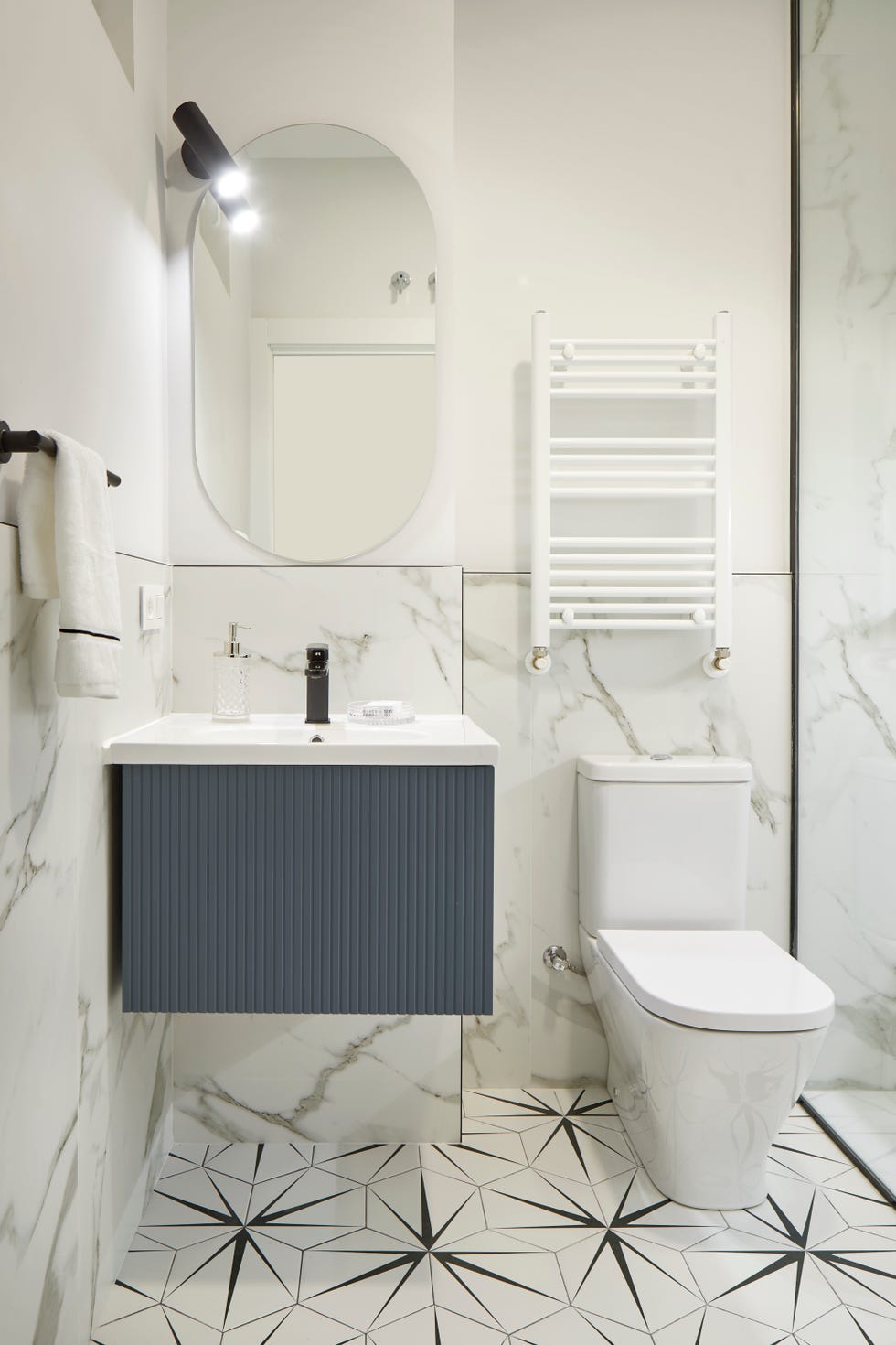 baño revestido con mármol, suelo con azulejos geométricos y mueble de lavabo azul suspendido