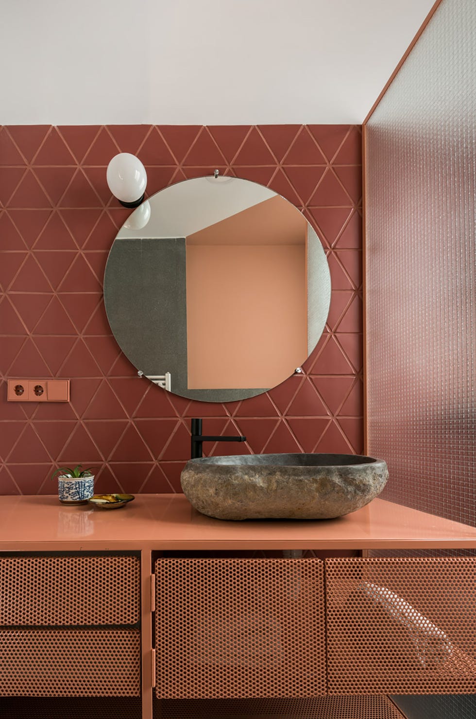 baño con pared de azulejos terracota, mueble de lavabo de rejilla en color salmón, y pila de piedra