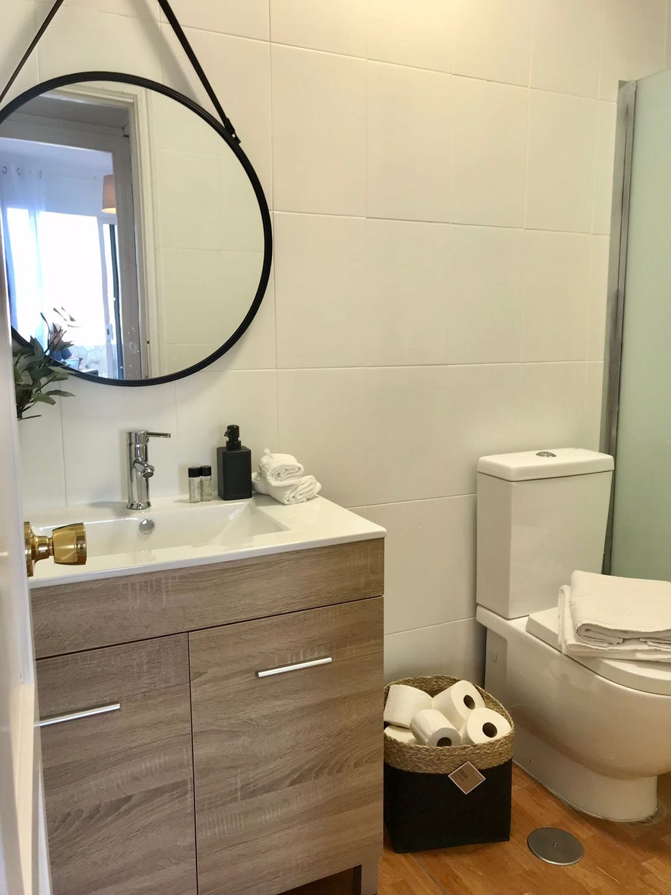 baño con mueble de madera y espejo redondo con marco metálico negro y correa