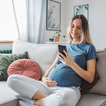 young pregnant woman at home sat on the sofa with a hand on her bump