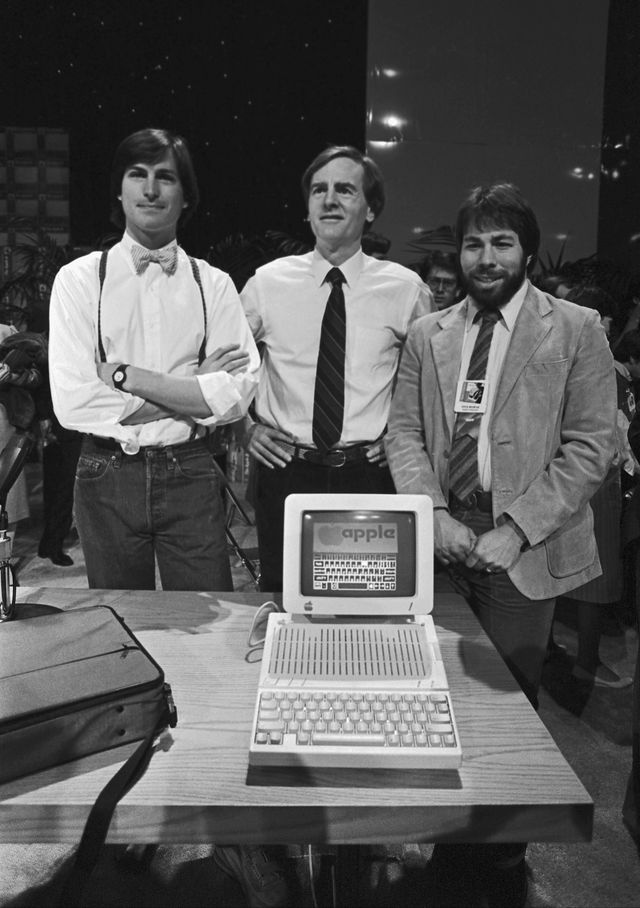 steve jobs, john sculley and steve wozniak smile behind a new apple computer in 1984